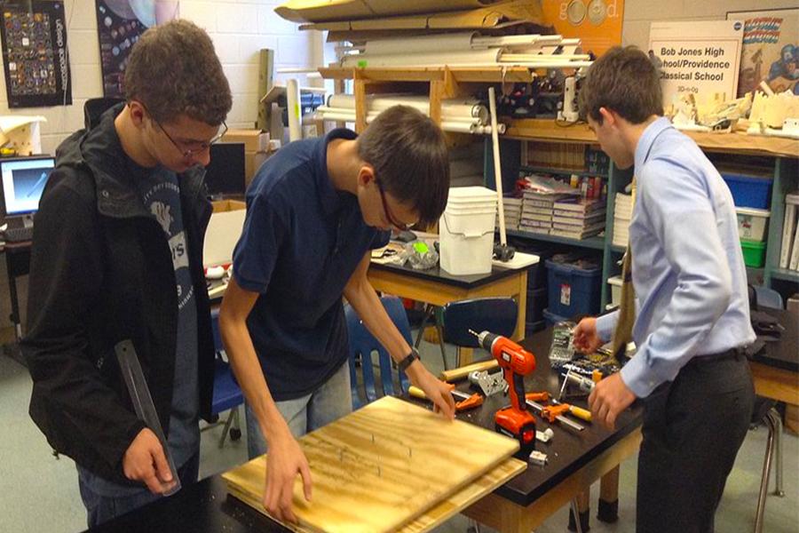 team members use power tools to assemble their robot.