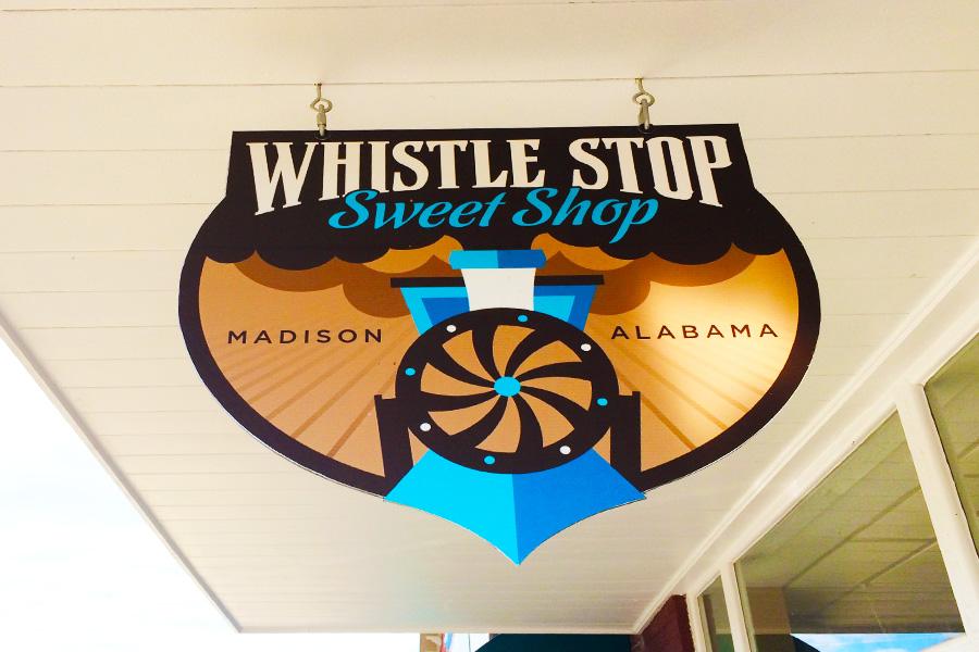 The Whistle Stop Sweet Shop sign that hangs outside of the store.